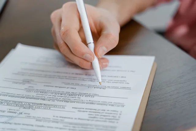 A hand holding a pen signing a document, close-up shot with focus on the paper. Flooring Change Order Pricing: How to Charge for Scope Creep